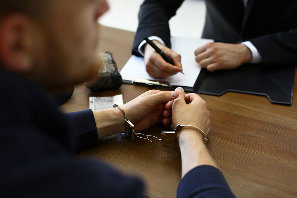 Zwei Personen im Gespräch. Verteidiger und Angeklagter mit Handschellen.